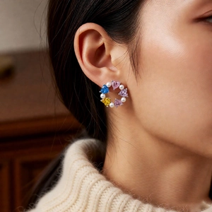 Close-up of model wearing colorful heart-shaped gemstone and pearl hoop earrings