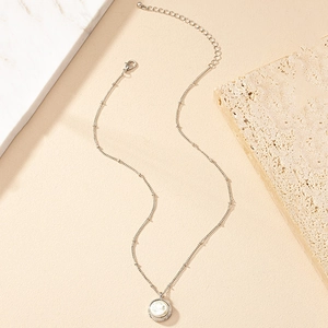 Élégant collier en chaîne argentée avec pendentif perle blanche sur surface en marbre