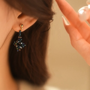 Detail of beaded flower earrings with iridescent dark beads and gold metal accents on model