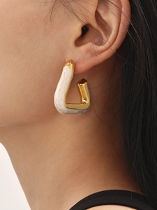 Detailed close-up of golden triangular hoop earrings with cream marble inlay on model's ear