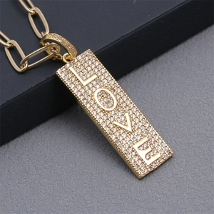 Close-up of gold rectangular pendant with LOVE lettering and pave-set crystals on a cuban chain