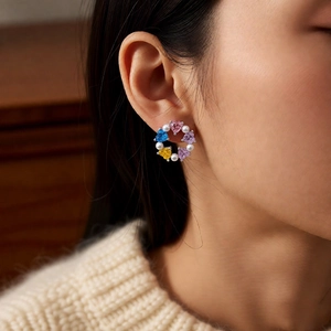 Macro detail of silver needle earrings with colorful zircon hearts and pearls on model