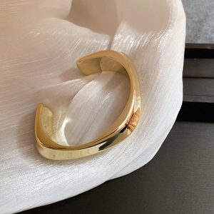 Vue détaillée du bracelet jonc doré torsadé sur un élégant tissu blanc texturé