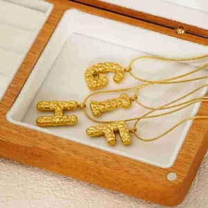 Detail of 18k gold plated necklaces with lava texture letter pendants in a wooden box