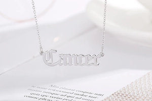 Macro detail of silver Cancer zodiac pendant with vintage gothic font on minimalist chain