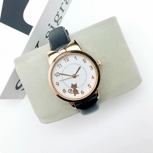 Detail of gold cat watch with black leather strap on display pillow for girls