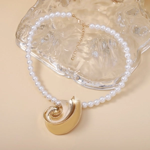Detailed close-up of a white pearl necklace with a large golden shell-shaped metal pendant