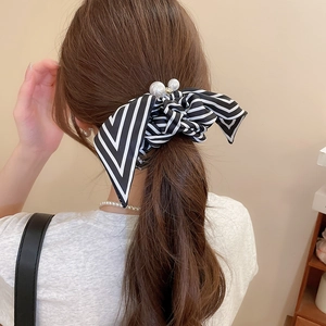 Detail of striped bow hair tie with white faux pearls worn in a low ponytail