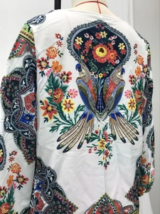 Détail du motif bohème sur chemisier blanc en mousseline avec perroquets et fleurs
