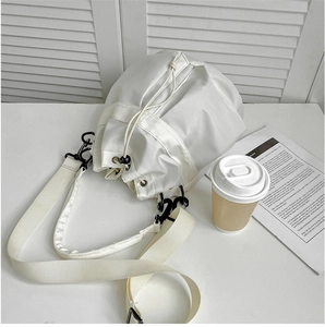 White drawstring bucket bag made of smooth nylon fabric on a table with a lifestyle setting
