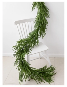 Realistic Norfolk pine garland draped on a white chair for Christmas indoor decoration