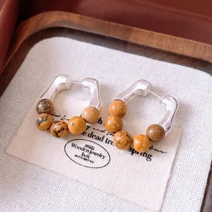 Silver vintage hoop earrings with brown stone beads on a beige woven texture background