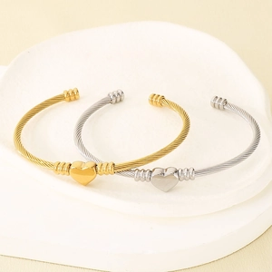 Détail de bracelets torsadés à cœur or et argent sur un socle d'exposition en pierre