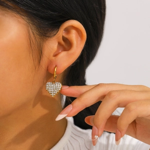 Elegant gold heart earrings with full rhinestone pavé shown on a model's ear