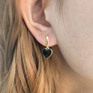 Close-up of golden hoop earrings with black enamel heart charms worn on ear