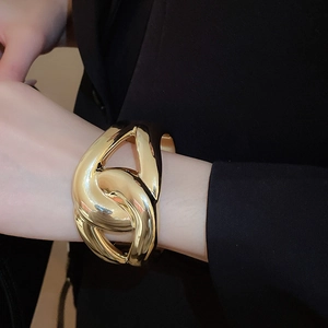 Detail shot of wide twisted gold bangle with high-polished finish on a black suit sleeve