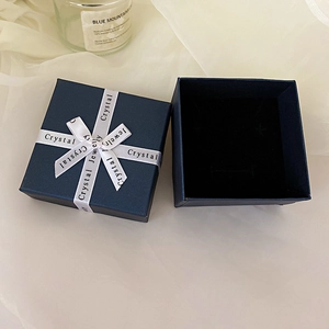 Detail of dark blue jewelry box with white satin bow and black velvet lining