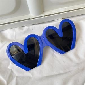 Flat lay view of heart-shaped sunglasses with blue frames and black lenses on fabric