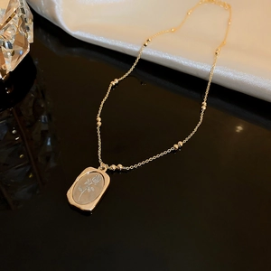 Close-up of golden beaded chain necklace with square rose relief pendant on silk fabric