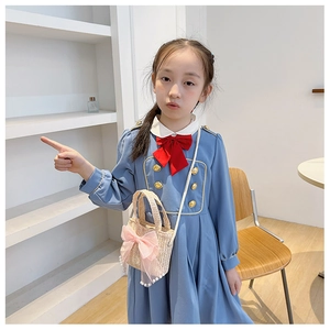 Detail of child wearing blue dress and straw cross-body bag with pink bow and pearls