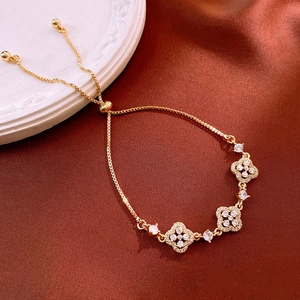 Detail of gold-plated clover bracelet with white zircon inlay on red silk background