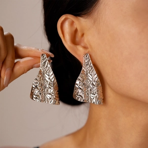 Gros plan d'une boucle d'oreille géométrique en argent avec texture métallique plissée