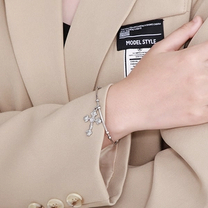 Detailed view of silver cross bracelet with rose and heart motifs on a model wrist