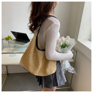Detail of a beige woven straw shoulder bag with black trim in a lifestyle setting