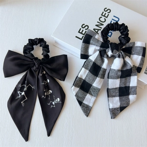 Detail of satin skull print and checkered pattern bow scrunchies on white surface
