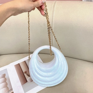 Detail of pearlescent white acrylic wave bag with gold chain on a beige sofa background