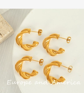 Detail view of gold twisted C-shaped hoop earrings on white stone background