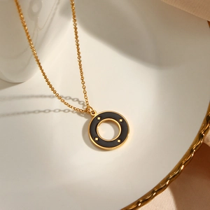 Close-up of golden necklace with black round pendant featuring four gold star patterns