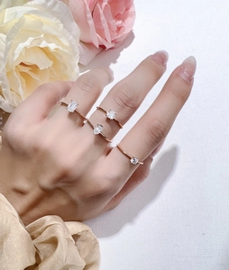 Detailed view of rose gold rings with emerald cut zircons worn on a hand with flowers