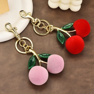 Plush red and pink cherry keychains with gold metal leaves on a leather surface