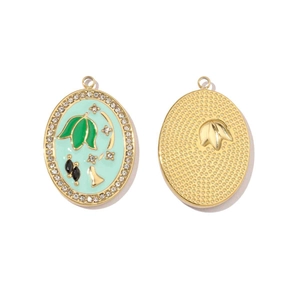 Detail view of oval gold pendants with green enamel leaf patterns and rhinestone edges