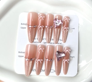 Detail of champagne cat-eye press-on nails with pink bows and heart crystal accents