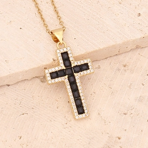 Minimalist gold cross necklace with black zircon inlay on a textured stone surface