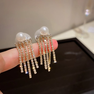 Detail of elegant pearl earrings with sparkling rhinestone tassels held by hand