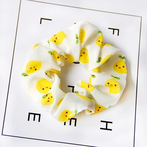 Detail shot of white fabric scrunchie with yellow lemon patterns on a white background