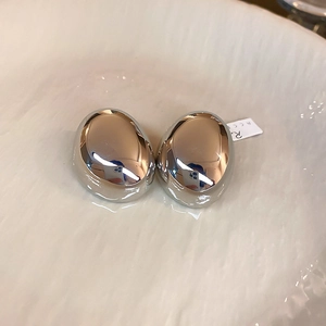 Macro shot of silver-colored oval drop earrings with a polished mirror finish on ceramic
