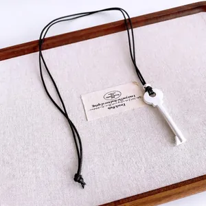 Minimalist vintage key pendant necklace with black leather cord on a linen texture tray