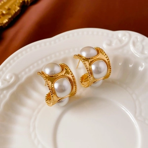 Macro shot of vintage C-shaped gold pearl earrings with beaded edge detail on a tray