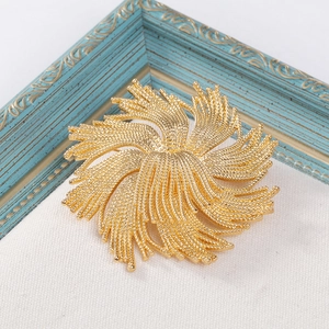 Vintage golden fireworks brooch with intricate floral design on beige textured fabric