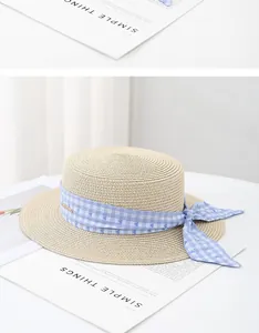 Detail of a boater straw hat featuring a blue plaid ribbon and delicate heart bow