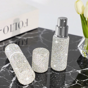 Sparkly rhinestone-covered travel perfume spray bottle on a marble surface with flowers