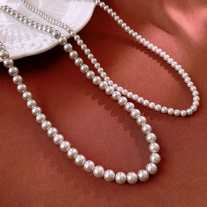 Macro shot of two creamy white pearl necklaces displayed on rich red silk fabric background