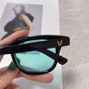 Detail of black square frames with light green lenses and golden V-shaped metal logo