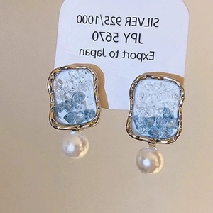 Detail of silver 925 earrings with blue crystals and hanging white pearls on paper card