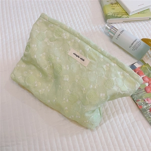 Close-up of green cosmetic bag with 3D floral texture and 'simple wish' woven label