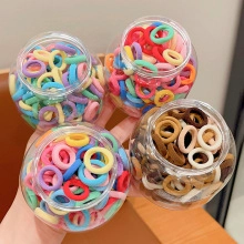 Dettaglio di quattro vasetti pieni di elastici per capelli in nylon colorati e terra